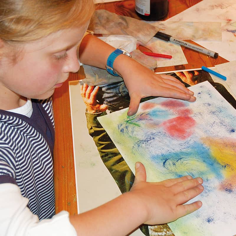 A child paints with Seccorell paints on a sheet of paper. He uses his fingers to incorporate the colors and create a vivid picture.
